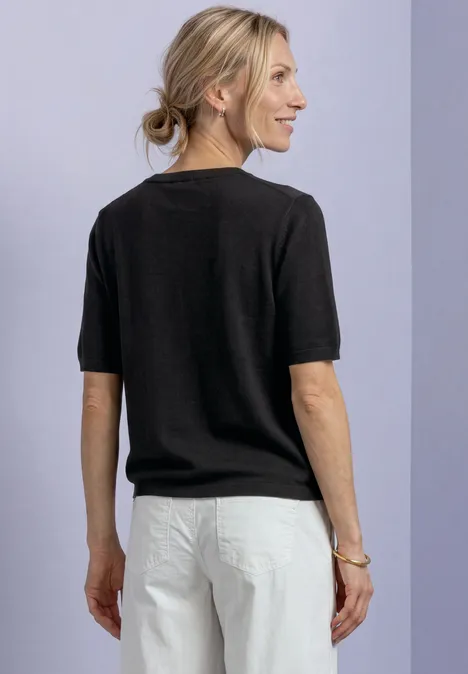 T-shirt met korte mouwen en ronde hals in effen kleur Black Vrouw van achteren, met zwart T-shirt met korte mouwen en witte broek, blond haar in lage paardenstaart.