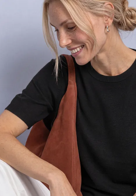 T-shirt met korte mouwen en ronde hals in effen kleur Black Een jonge blondine met zwart T-shirt en bruine schoudertas, glimlacht en kijkt schuin naar beneden.