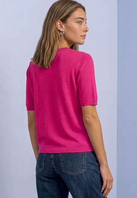 Vrouw van achteren in een korte roze trui en jeans voor een lichte achtergrond.