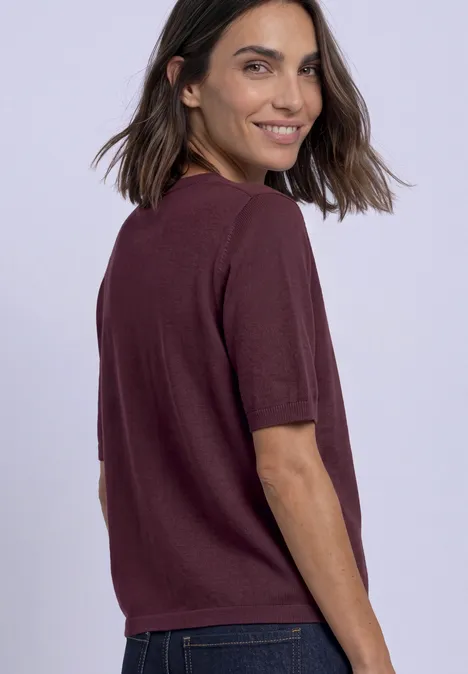 Vrouw in paars T-shirt glimlacht en kijkt over haar schouder