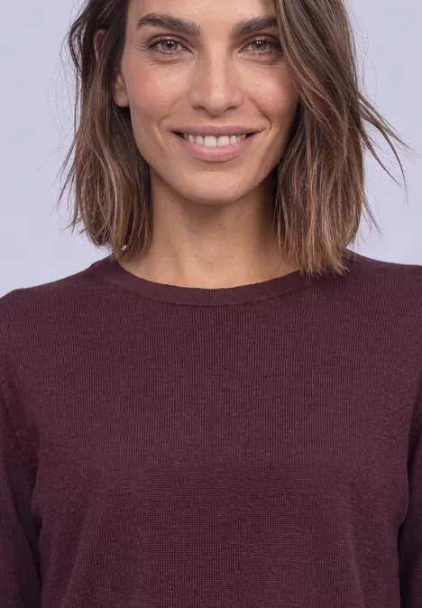 Close-up van een glimlachende vrouw met halflang haar en bordeaux shirt tegen een lichte achtergrond