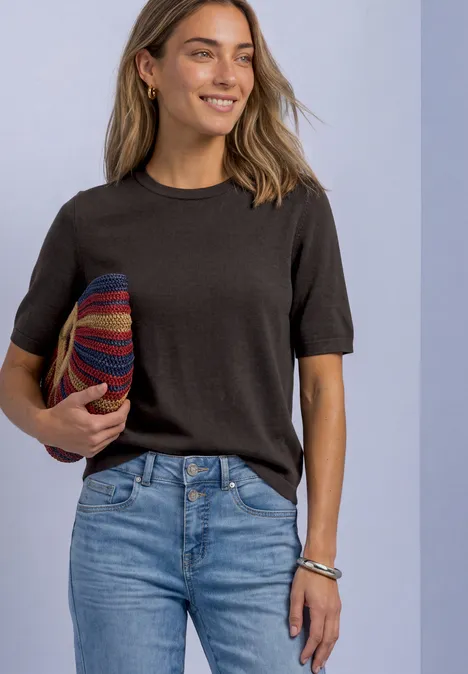 T-shirt met korte mouwen en ronde hals in effen kleur black coffee Vrouw in zwart T-shirt en jeans houdt kleurrijke hoed vast en lacht.