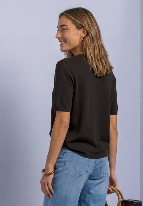 T-shirt met korte mouwen en ronde hals in effen kleur black coffee Vrouw van achteren in zwart T-shirt en blauwe jeans met strooien tas, glimlachend zijwaarts kijkend