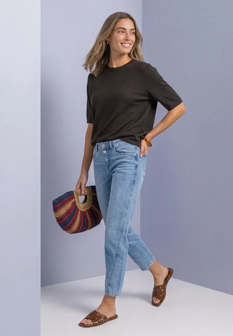 T-shirt met korte mouwen en ronde hals in effen kleur black coffee Vrouw lacht in zwart T-shirt, lichtblauwe jeans en bruine sandalen, met een kleurrijke tas.