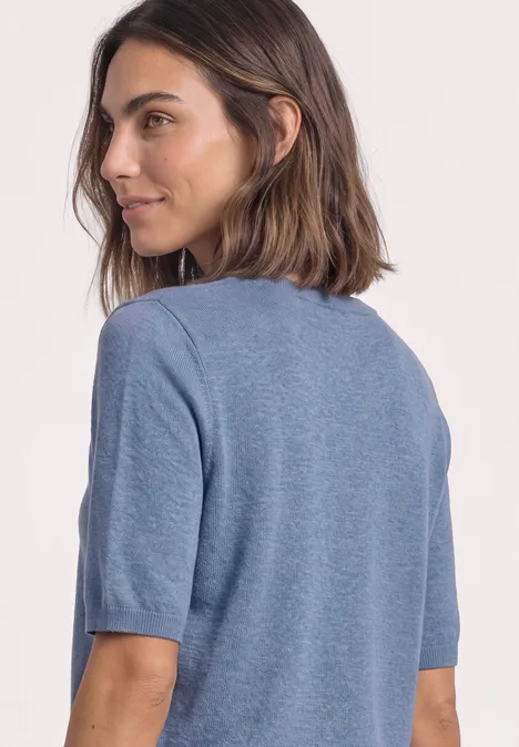 Een vrouw met halflang bruin haar kijkt opzij en draagt een lichtblauw T-shirt.