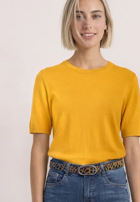 T-shirt met korte mouwen en ronde hals in effen kleur saffron yellow Vrouw lacht, draagt gele korte mouwtrui en spijkerbroek met patroonriem tegen lichte achtergrond.