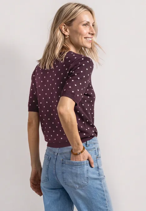 Trui met korte mouwen, ronde hals en patroon rustic rouge Een vrouw in jeans en een gestipt shirt kijkt glimlachend over haar schouder.