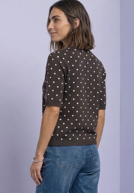 Vrouw in een polkadot trui met korte mouwen en spijkerbroek, zijwaarts.