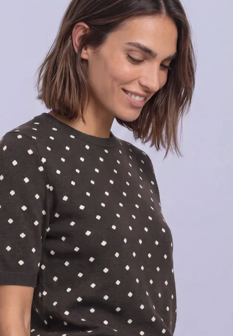 Vrouw glimlacht in bruin polkadottrui, zijaanzicht.