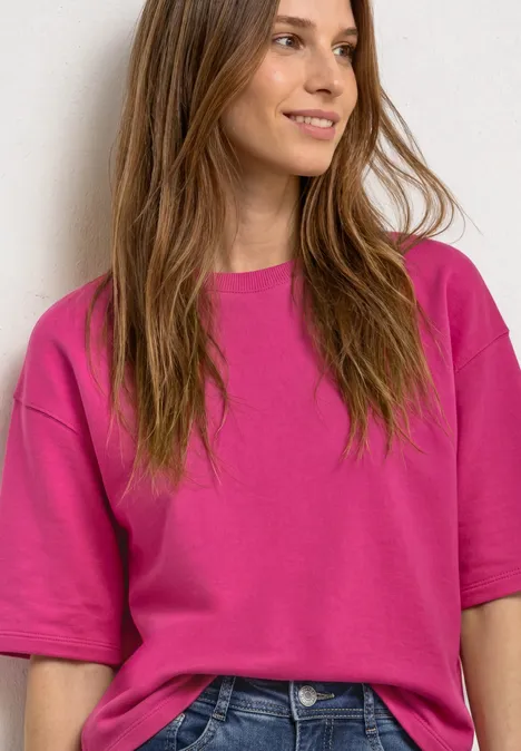 Sweatshirt met korte mouwen en ronde hals magenta dream Junge Frau mit locker sitzendem pinkfarbenem T-Shirt lächelt seitlich.