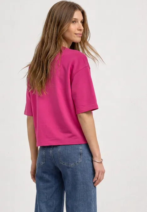 Sweatshirt met korte mouwen en ronde hals magenta dream Eine Frau steht im Profil, trägt ein pinkes Shirt und blaue Jeans und blickt über ihre Schulter.