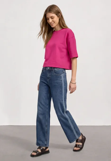 Sweatshirt met korte mouwen en ronde hals magenta dream Eine Frau trägt ein pinkes Oberteil, weite Jeans und schwarze Sandalen vor weißem Hintergrund.
