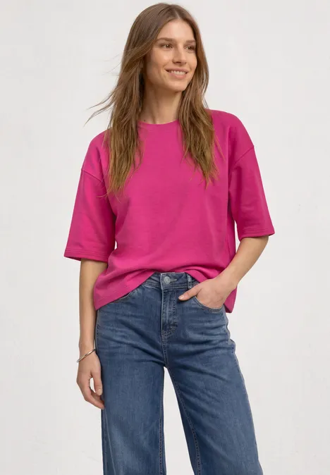 Sweatshirt met korte mouwen en ronde hals magenta dream Eine lächelnde Frau in pinkem T-Shirt und blauen Jeans steht lässig.