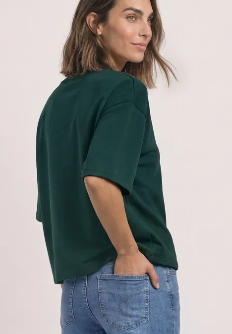 Sweatshirt met korte mouwen en ronde hals shadow teal Frau in grünem T-Shirt und blauen Jeans, seitlich mit Händen in Hosentaschen.