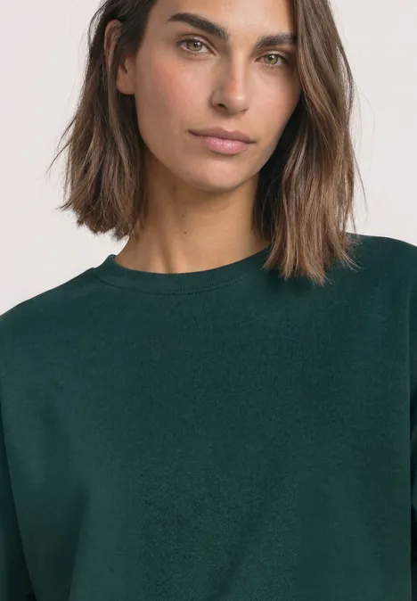 Sweatshirt met korte mouwen en ronde hals shadow teal Porträt einer Frau mit schulterlangen Haaren und dunkelgrünem Pullover vor neutralem Hintergrund.