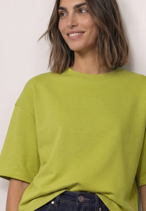 Sweatshirt met korte mouwen en ronde hals apple lime Eine lächelnde Frau trägt ein lockeres, kurzärmeliges, hellgrünes Shirt.
