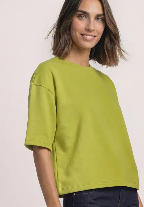 Sweatshirt met korte mouwen en ronde hals apple lime Eine lächelnde Frau mit schulterlangen dunklen Haaren trägt ein locker geschnittenes, hellgrünes T-Shirt.