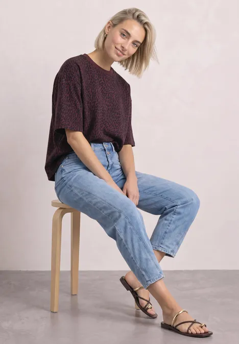 Bluza z krótkim rękawem i okrągłym dekoltem rustic rouge Młoda kobieta siedzi na stołku w jeansach i krótkim sweterku, uśmiechając się do aparatu.