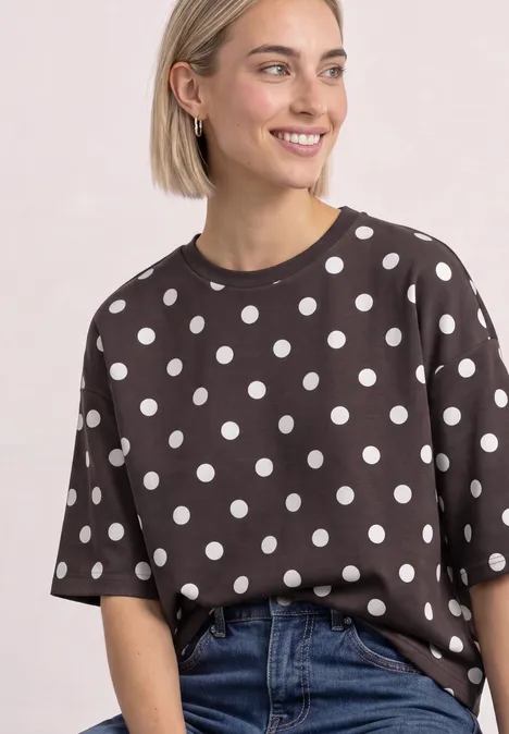 Lächelnde Frau in schwarzem T-Shirt mit weißen Punkten und blonden Haaren, kombiniert mit blauer Jeans.