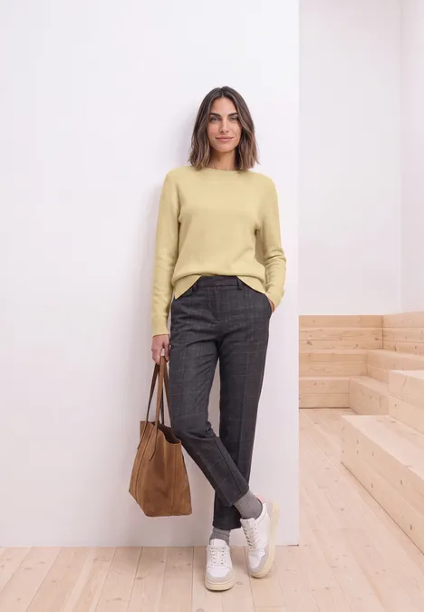 Pull à manches longues et col bateau sunbeam yellow mel. Femme en pull clair, pantalon foncé et baskets blanches, sac marron, pose décontractée dans un intérieur moderne.
