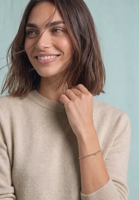 Pull à manches longues et col bateau clay sand mel. Une femme aux cheveux bruns porte un pull beige, souriant de côté sur fond clair.