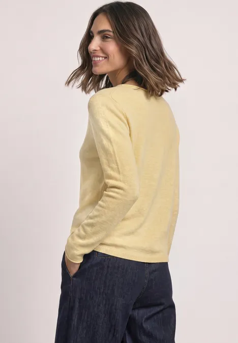Femme portant un pull jaune et un pantalon foncé, regard souriant de profil.