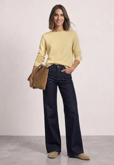 Femme en pull jaune, jean large bleu foncé, mocassins beiges et sac marron.