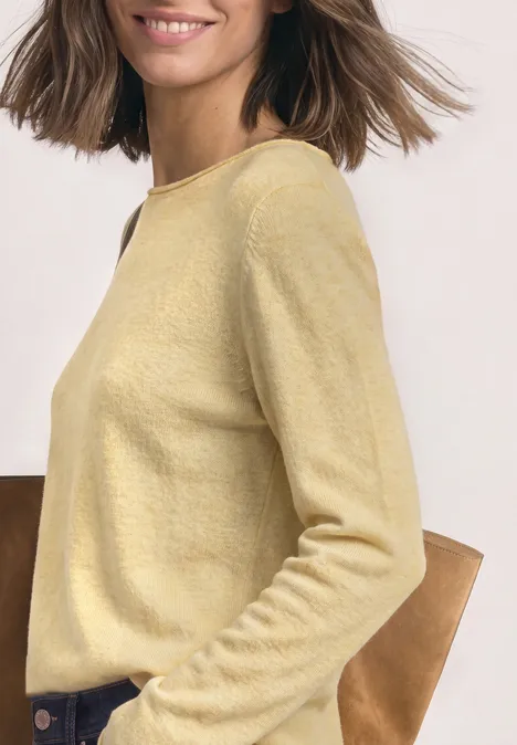Femme de profil portant un pull jaune clair, sourire naturel, style décontracté et élégant.