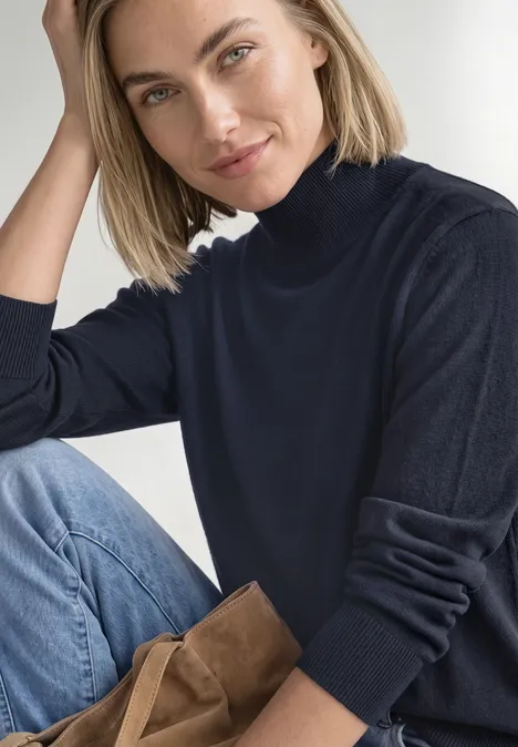 Basic Pullover mit Turtle Neck darkest blue Frau mit hellem Haar in dunklem Rollkragenpullover sitzt entspannt und lächelt.