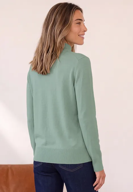 Basic Pullover mit Turtle Neck eucalyptus green Frau von hinten in grünem Pullover und Jeans, lächelt seitlich vor hellem Hintergrund.