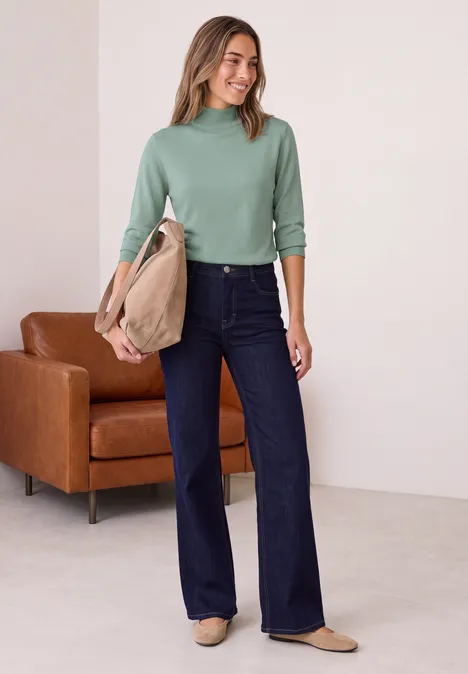 Basic Pullover mit Turtle Neck eucalyptus green Frau in grünem Rollkragenpullover, weiten dunkelblauen Jeans und beiger Schultertasche