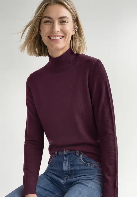 Basic Pullover mit Turtle Neck berry maroon Eine lächelnde Frau in bordeauxrotem Rollkragenpullover und blauen Jeans.