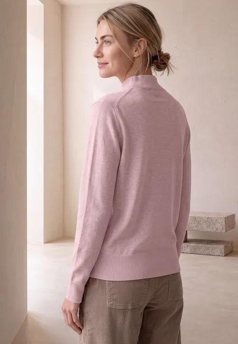 Basic Pullover mit Turtle Neck quiet rose mel. Frau im Profil mit rosafarbenem Pullover und beigen Hosen, steht in hellem Raum vor einem Fenster.