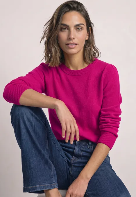 Langarm Pullover mit Rundhals und Raffung magenta dream Frau mit pinkem Pullover und Jeans sitzt entspannt mit übergeschlagenem Bein, schaut lächelnd in die Kamera.