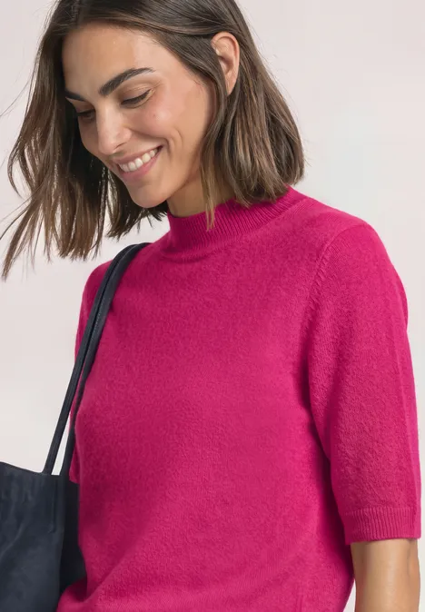 Frau in pinkem Kurzarm-Pullover mit Umhängetasche, lächelnd