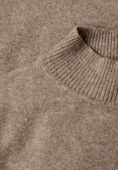 Nahaufnahme eines beigefarbenen, gestrickten Wollpullovers mit Rundhalsausschnitt.