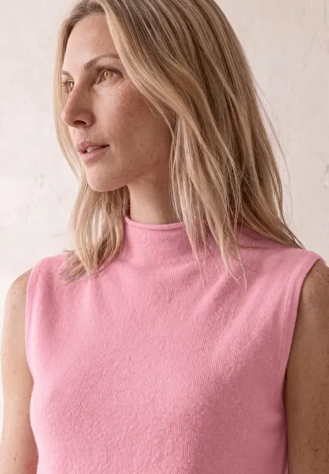 Une femme blonde en top rose sans manches regarde sur le côté vers la gauche.