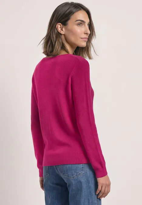 Femme de dos en pull rose vif et jean sur fond clair.