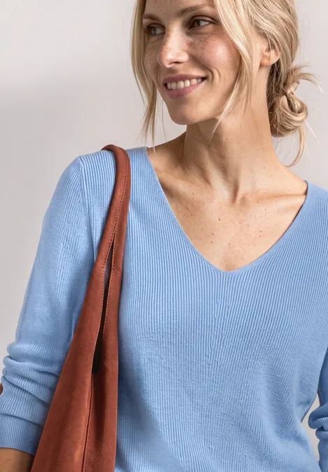 Eine blonde Frau in einem hellblauen Pullover mit brauner Tasche über der Schulter.