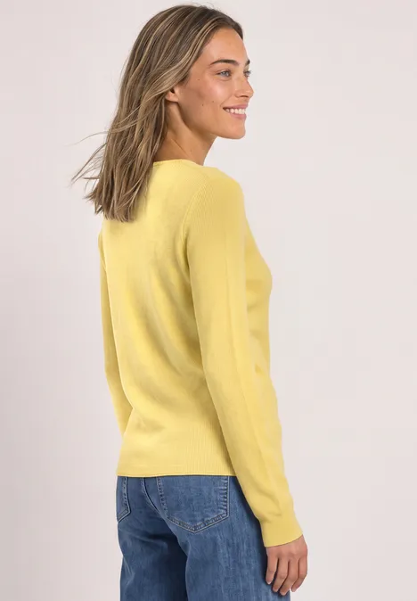 Femme en pull jaune et jean, vue de profil, souriante.