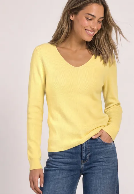 Femme souriante en pull jaune à col en V et jean bleu.