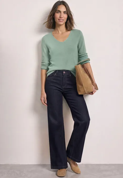 Eine Frau in weiter dunkelblauer Jeans und mintgrünem Pullover hält eine Tasche.