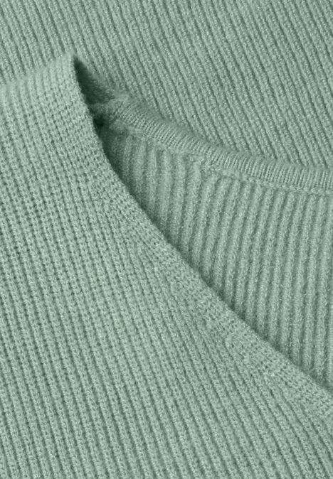 Nahaufnahme eines hellgrünen, gerippten Strickpullovers mit V-Ausschnitt.