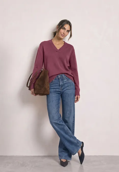 Vrouw met bordeauxrode trui, wijde jeans en tas