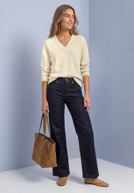 Femme en pull col V crème, jean large bleu foncé, mocassins beiges et sac marron sur fond uni.