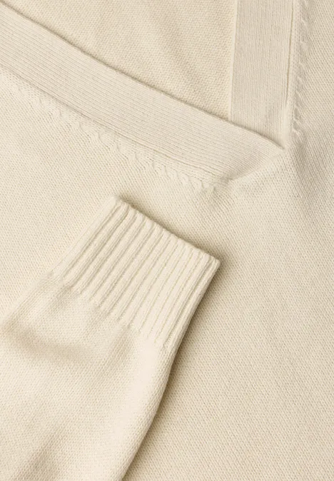Gros plan sur un pull en maille crème à col V et poignets côtelés.