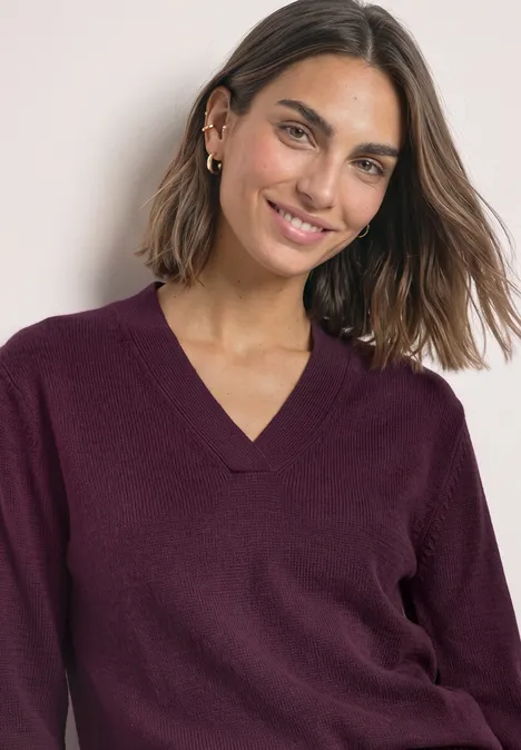 Femme aux cheveux mi-longs portant un pull bordeaux à col en V, souriante face à l’objectif.