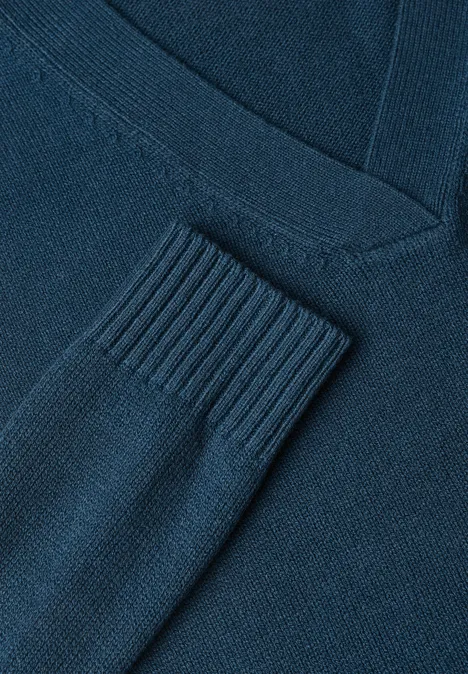Gros plan d’un pull en maille bleu foncé à col V avec bord-côtes sur la manche.
