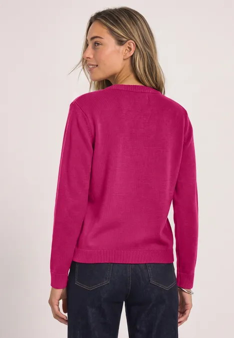 Vrouw van achteren met roze trui en donkerblauwe jeans tegen lichte achtergrond.