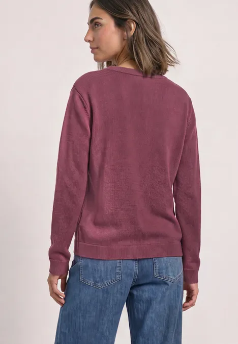 Vrouw gezien van achteren, kort haar, paarse trui en blauwe spijkerbroek, lichte achtergrond.